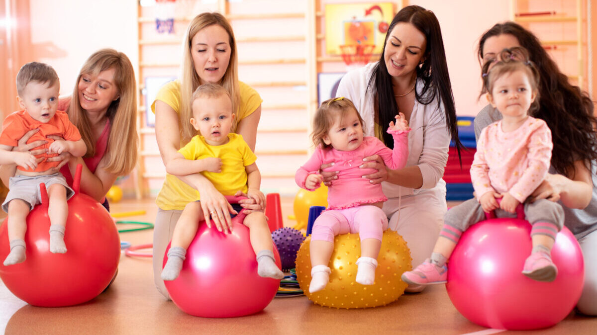 Group of young moms and their babies doing yoga exercises on gymnastic balls at fitness gym